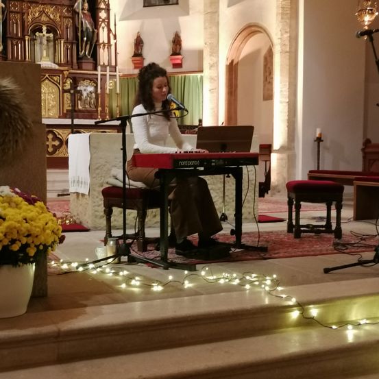 Eine Frau spielt ein Keyboard in einer Kirche mit einem Mikrofon und Blumen auf der Bühne.