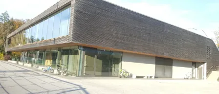 Die Vorderseite eines modernen Gebäudes mit großen Fenstern und vor dem Gebäude geparkten Fahrrädern.