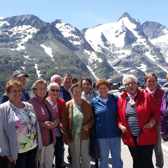 Eine Gruppe von Menschen steht vor einem Berg mit Schnee auf den Gipfeln. Sie lächeln und posieren für ein Foto.