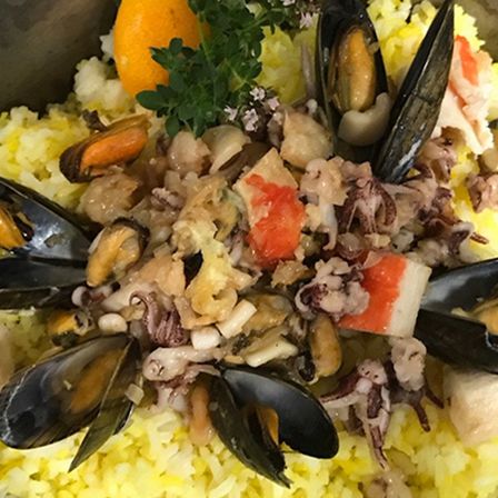 Eine Schüssel mit Reis und Meeresfrüchten, garniert mit Muscheln, Krabbenfleisch und einer Orangenscheibe, verziert mit grünen Kräutern.