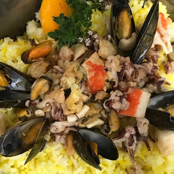 Eine Schüssel mit Reis und Meeresfrüchten, garniert mit Muscheln, Krabbenfleisch und einer Orangenscheibe, verziert mit grünen Kräutern.