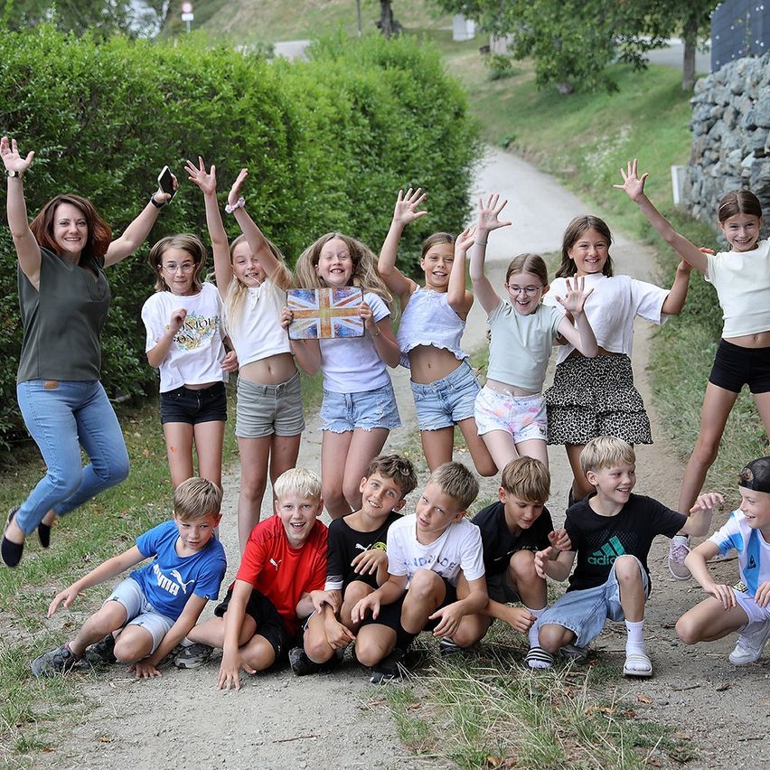 Eine Gruppe von Kindern und einer erwachsenen Frau posiert für ein Foto auf einem Feldweg mit Grünpflanzen im Hintergrund.