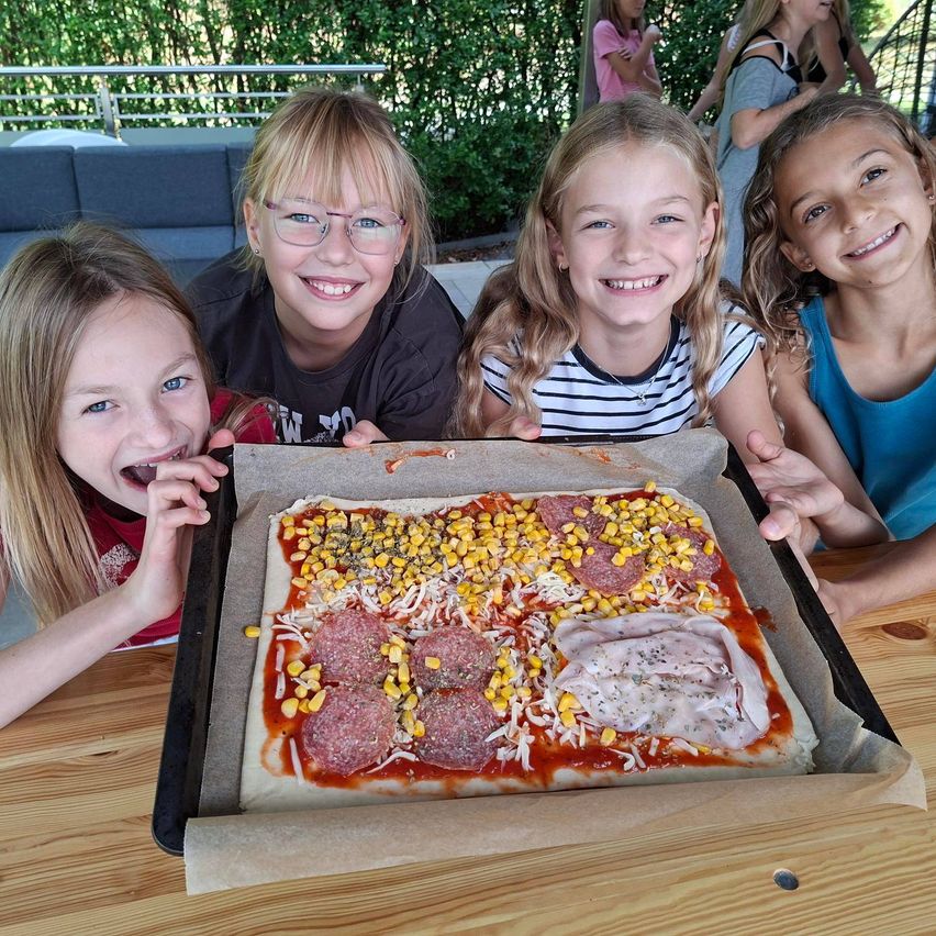 Vier Mädchen präsentieren eine belegte Pizza im Freien