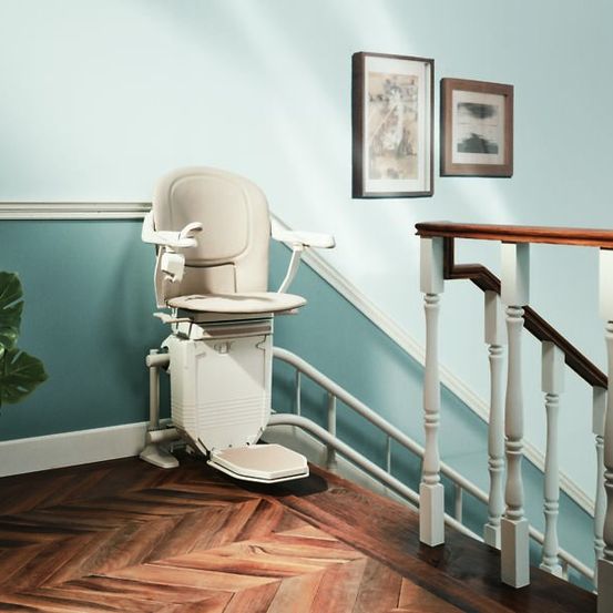 Ein elektrischer Treppenlift ist an den Stufen installiert, mit einem Topfpflanzen links und zwei gerahmten Bildern an der Wand.