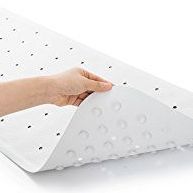Ein weißer Badematten mit kleinen Saugnäpfen wird von einer Hand gehalten. Die Matte liegt auf einer weißen Oberfläche.