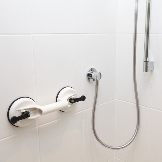 Eine weiße Badezimmerwand mit einem silbernen Duschschlauch, einem Handtuchhalter und einem Chrom-Duschgriff.