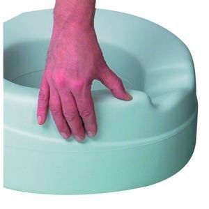 Eine Hand hält den Rand einer weißen, zylindrischen Toilette. Die Toilette ist für einfaches Benutzen von Personen mit eingeschränkter Mobilität konzipiert.