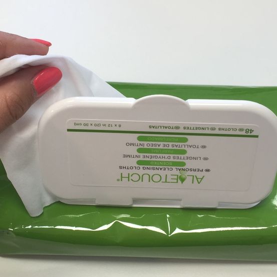 Eine Hand hält ein weißes Tuch über einem grünen Behälter, der mit 'ALERT' und grünem Text auf einer weißen Oberfläche gekennzeichnet ist.