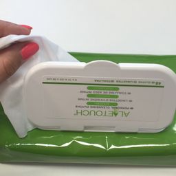 Eine Hand hält ein weißes Tuch über einem grünen Behälter, der mit 'ALERT' und grünem Text auf einer weißen Oberfläche gekennzeichnet ist.