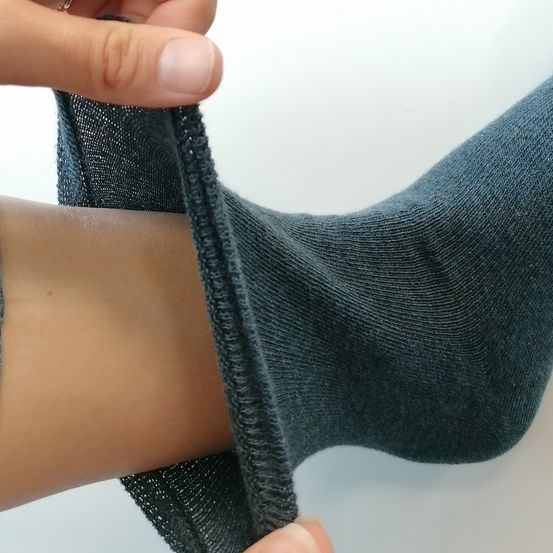Eine Person, die Jeans und einen Ring trägt, zieht einen blauen Socken an ihrem Bein hoch. Der Socke ist bis zum Knöchel umgeschlagen.