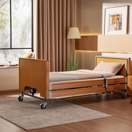 Ein Krankenhausbett mit Rädern steht in einem Zimmer mit einem Teppich auf dem Boden. Eine Lampe steht neben dem Bett, und ein Bilderrahmen ist an der Wand. Ein Fenster mit Blick auf Bäume draußen.