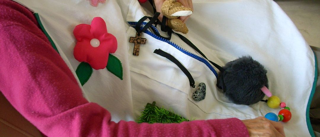 Eine ältere Person in einem rosa Pullover hält einen Kuschelhasen. Sie liegt auf einem Bett mit einem weißen Tuch, einem Kreuz, Blumen und einem Reißverschluss. Das Foto hat einen Datumsstempel vom 04/11/2011.