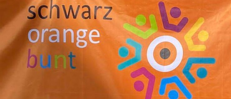 Ein orangefarbener Banner zeigt ein farbenfrohes Logo von Menschen und 'KO' in weiß. Darunter steht 'ZUSAM' und '175 Jahre'. Der Banner hat einen orangefarbenen Hintergrund.