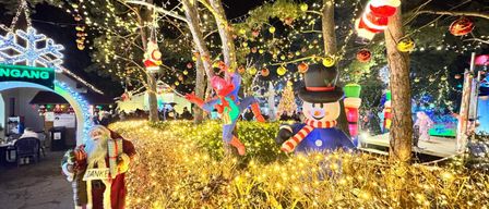 Ein nachtlicher Weihnachtspark mit Spiderman- und Weihnachtsmannfiguren, beleuchteten Baumen und bunten Lichtern.