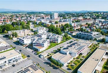 Luftaufnahme einer Stadt mit vielen Gebäuden, Bäumen und einer Straße. Der Himmel ist klar und das Gebiet ist von Bergen umgeben.