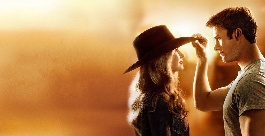 Eine Frau in einem Cowboyhut schaut einen Mann an, der ihren Hut mit seiner rechten Hand berührt.