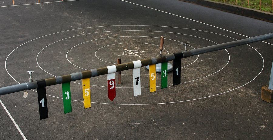 Ein Sportplatz mit schwarzem Asphalt und markierten Kreisen. Zahlen 1 bis 9 hängen an einer Stange.