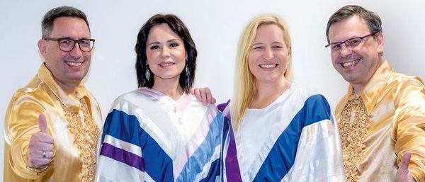 Vier Menschen, zwei Männer und zwei Frauen, gekleidet in passenden Kostümen mit weißen Stiefeln, lächeln und posieren für ein Foto.