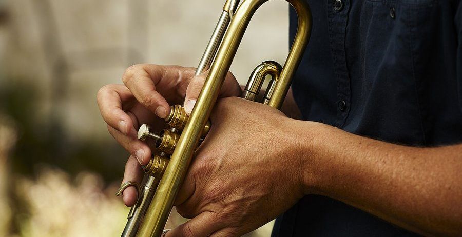 Eine Person hält eine Trompete mit beiden Händen und justiert die Ventile mit den Fingern. Die Trompete ist golden und die Hände der Person sind leicht verschwommen.