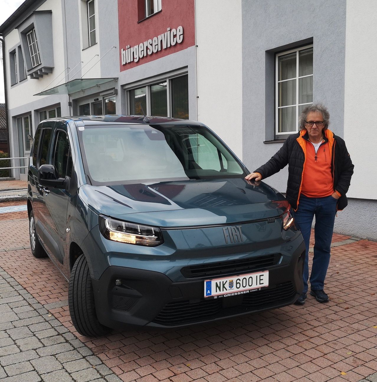 Ein Mann steht neben einem Fiat-Van mit dem Kennzeichen 'NK 600 IE' vor einem Gebäude mit dem Wort 'burgerservice'.