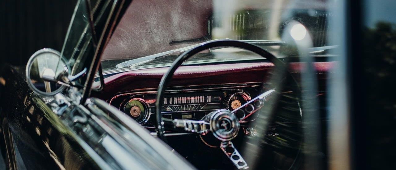 Nahaufnahme des Innenraums eines Oldtimers, mit Fokus auf dem Lenkrad und dem Armaturenbrett mit verschiedenen Anzeigen und Zifferblättern.