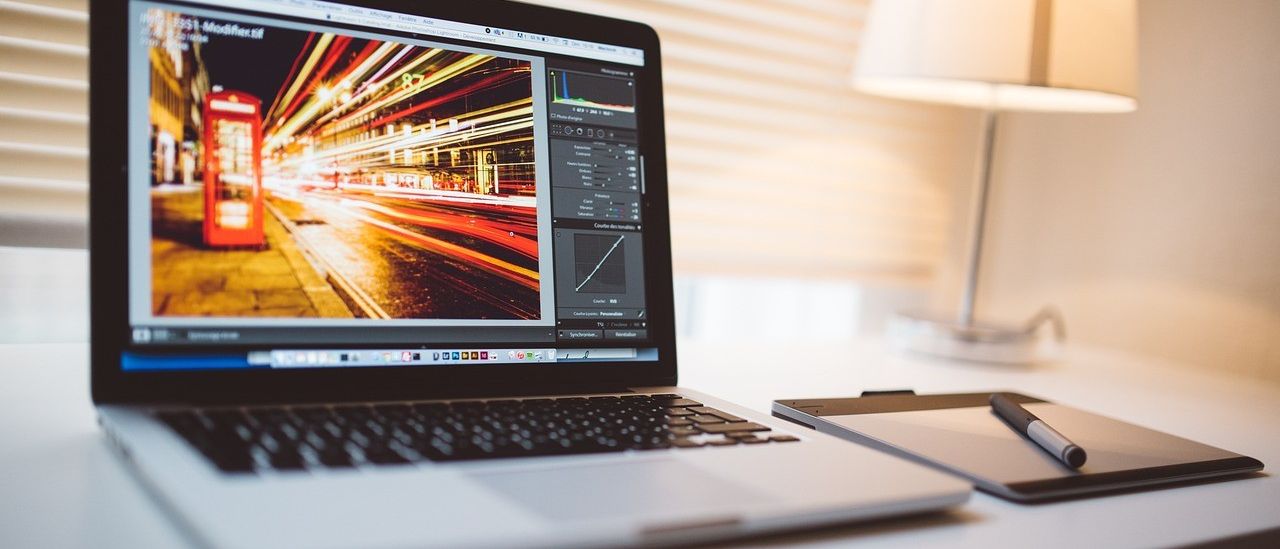 Offener Laptop auf einem Schreibtisch mit einem Stift und einem Tablet. Der Laptop-Bildschirm zeigt ein Bild einer Nachtstadt mit Lichtern.