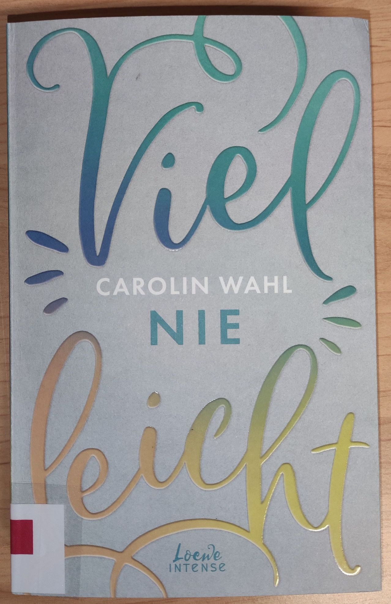 A book cover with the title 'Viel Nie Leicht' by Carolin Wahl, displayed on a wooden surface. The cover features a combination of teal, blue, and yellow fonts.