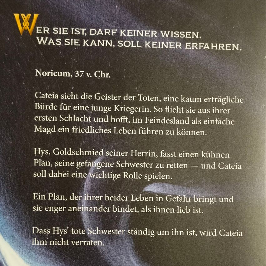A book page shows text in German. It reads about a character named Catia who sees the spirits of the dead and flees her homeland hoping for a peaceful life in the enemy's land. Hys, Catia's master, plans to rescue his captured sister, and Catia is to play a crucial role.