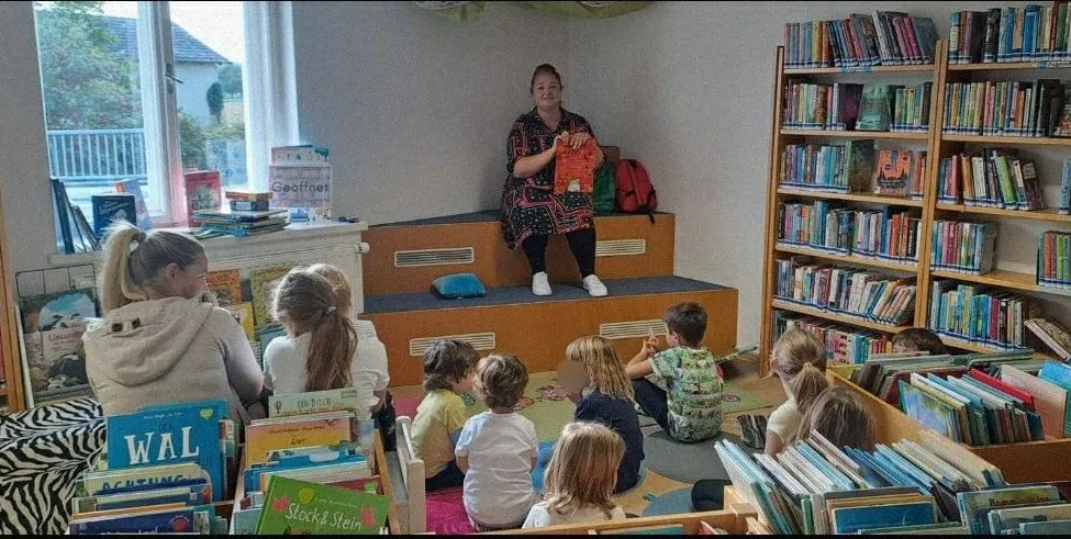Eine Frau liest ein Buch für eine Gruppe von Kindern in einer Bibliothek.