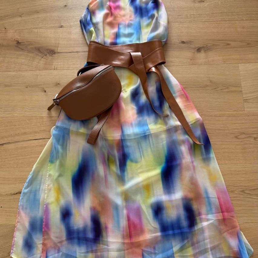 Ein farbenfrohes, tie-dye gemustertes Kleid mit einem braunen Gürtel und einer passenden Umhängetasche auf einem Holzboden.
