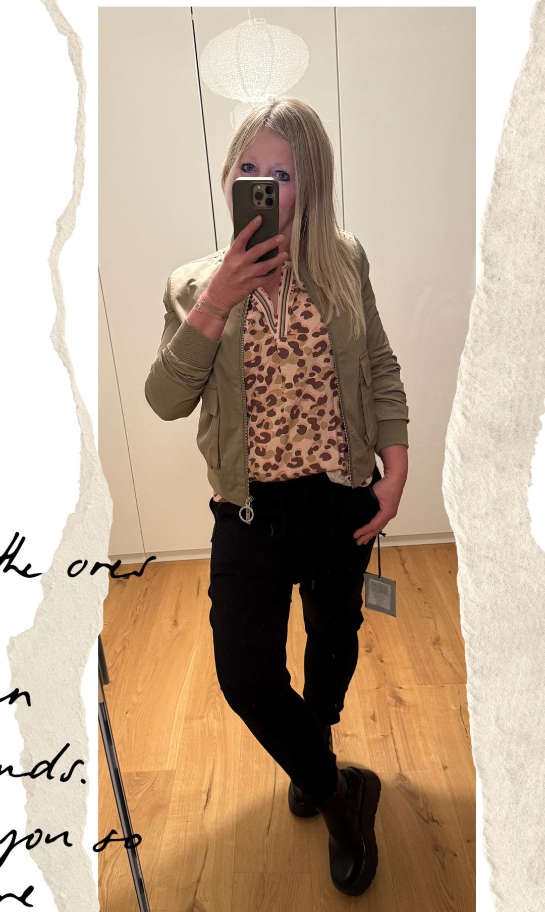 Eine Frau in einem Leopardenmuster-Blusen und einer khakifarbenen Jacke macht ein Selfie in einem Raum mit Holzboden.