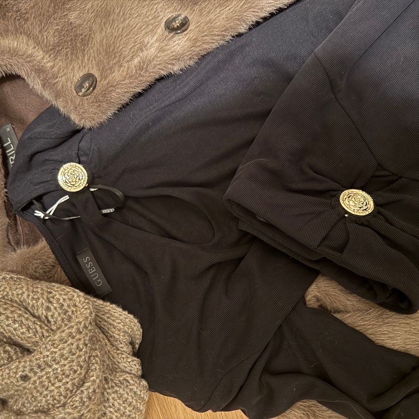 Ein Stapel Kleidung mit einem Pelzmantel, einem schwarzen Kleid und einem schwarzen Hemd mit goldenen Knöpfen.