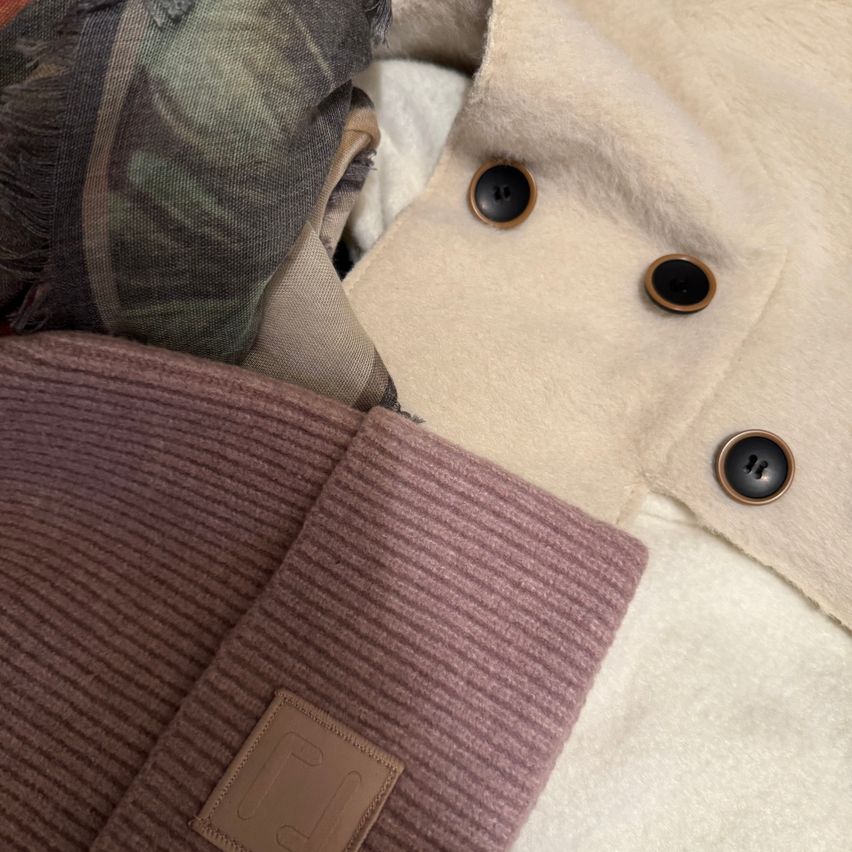 Eine Nahaufnahme von Kleidungsstücken mit einem beigen Mantel, einem lila gerippten Ärmel und einem Tarnkissen.