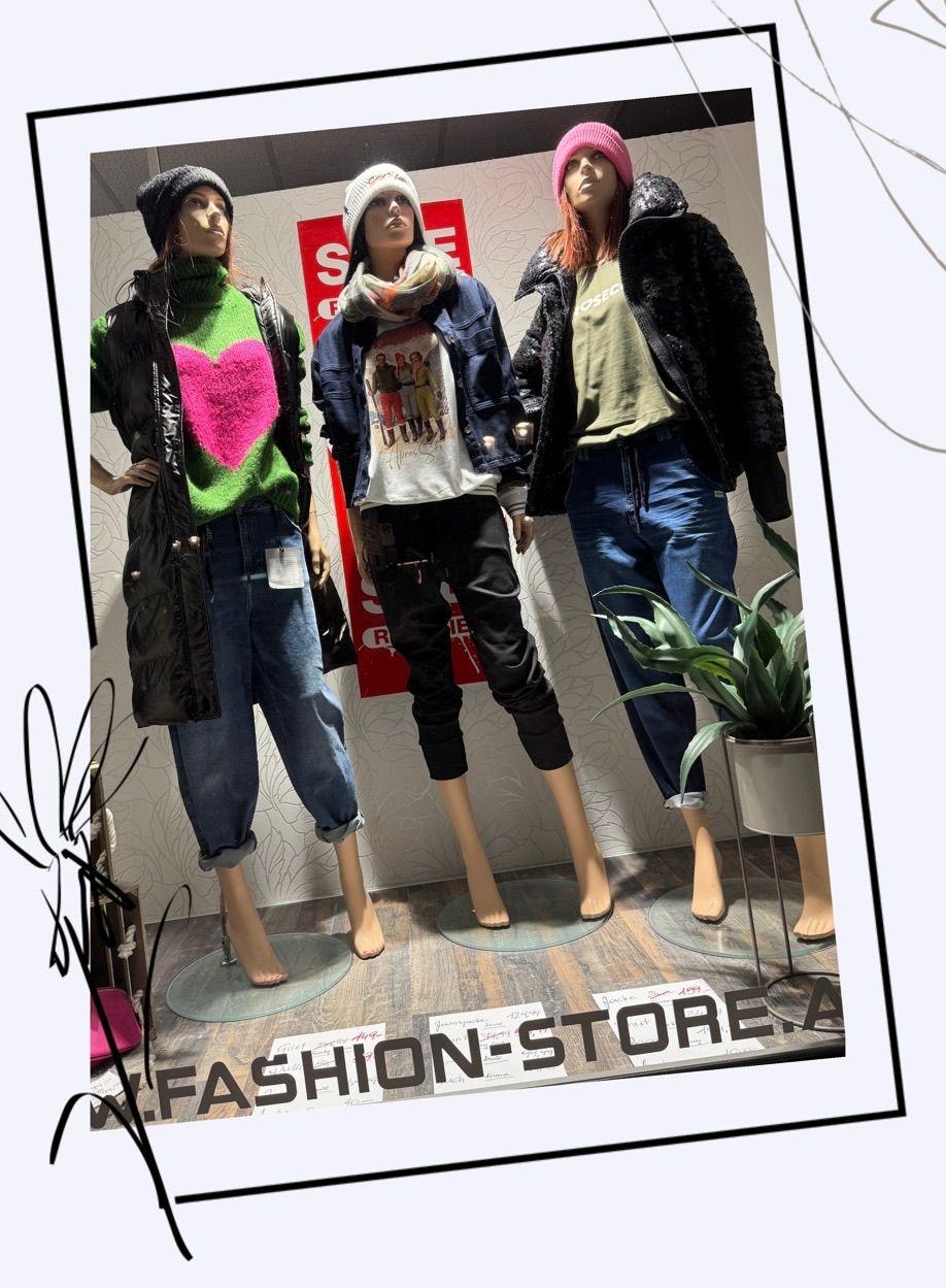 Drei Mannequins in Kleidungsstücken stehen in einem Geschäft, mit einer Topfpflanze neben ihnen. Die Mannequins tragen Winterkleidung, einschließlich Jacken, Schals und Jeans.
