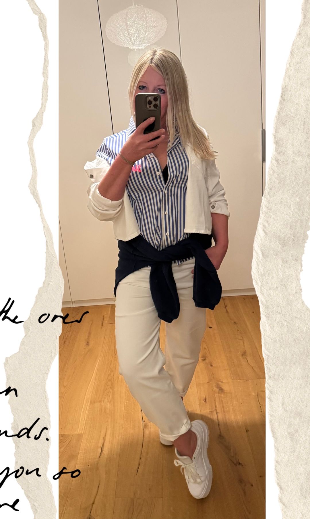 Eine Frau macht ein Selfie mit ihrem Handy. Sie trägt eine weiße Jacke über einem blau-weiß gestreiften Hemd. Sie hat beige Hosen mit einem blauen Gürtel.