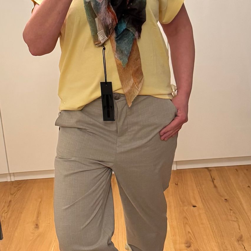 Eine Person in einem gelben Shirt und grauen Hosen steht in einem Raum und hält ein Tuch.