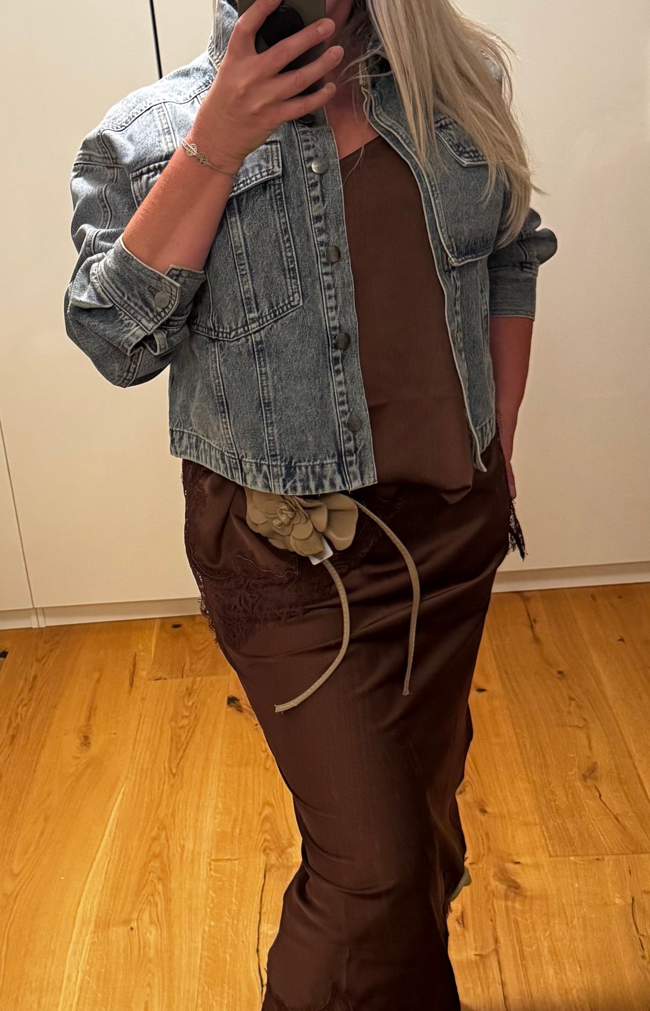 Eine Frau in einem braunen Oberteil und Rock, mit einer Jeansjacke und einer dekorativen Blume an der Taille.