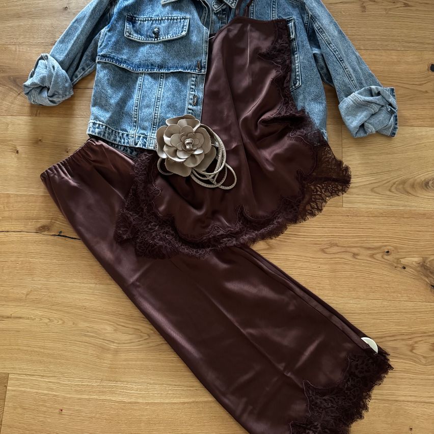 Ein brauner Seidenslip mit Spitzenbesatz und einer Jeansjacke auf einem Holzboden.