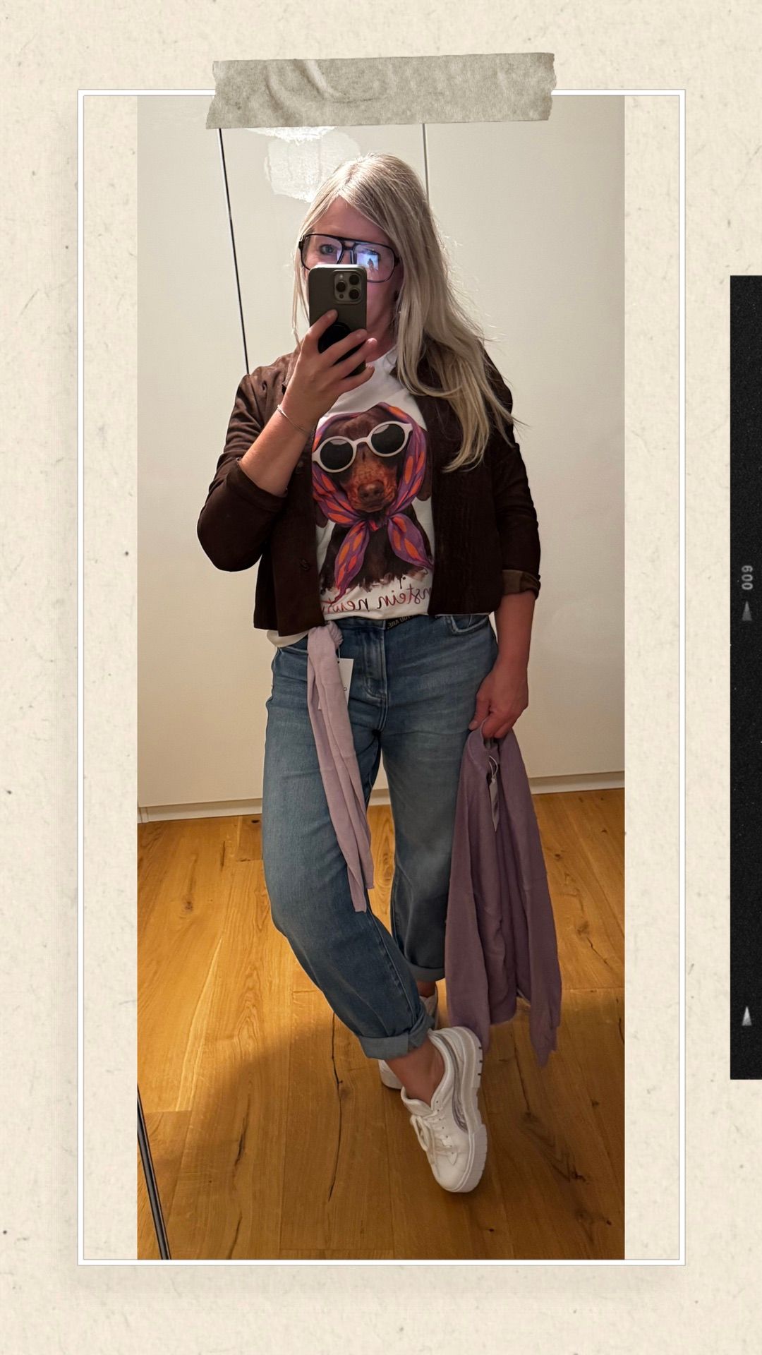 Eine Frau macht ein Selfie mit einem Hund, der eine Sonnenbrille auf ihrem Shirt trägt. Sie trägt eine braune Jacke und blaue Jeans.