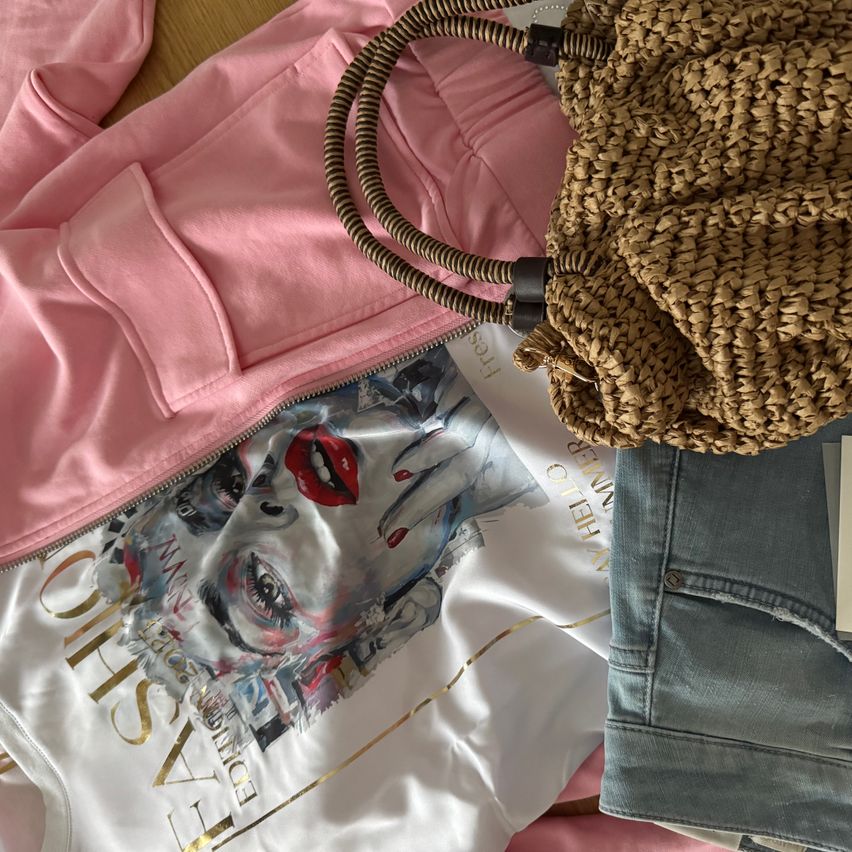A pink jacket, a white t-shirt with a Joker-inspired design, denim shorts, and a brown woven handbag. The t-shirt has a prominent 'CHIC EASY' gold text on the front.
