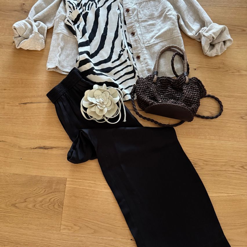 A zebra-patterned shirt, black pants, and a brown handbag are laid out on a wooden floor.