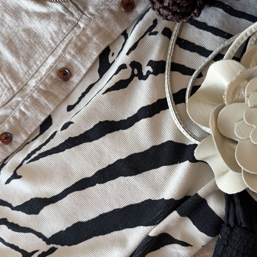 A white and black striped fabric with a white flower on the right. Above it, a beige jacket with brown buttons.
