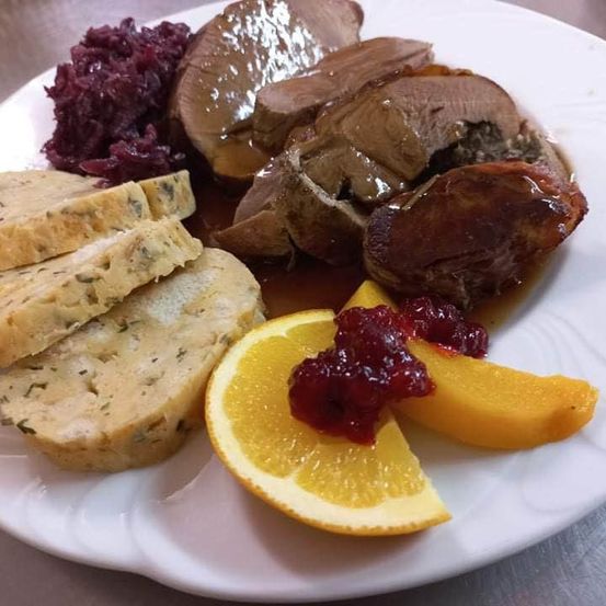 Ein weißer Teller mit geschnittenem Fleisch, Orangenscheiben und Cranberry-Sauce, zusammen mit einer Beilage aus Rotem Kohl.