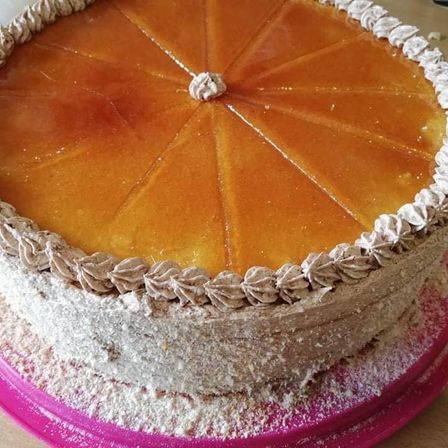 Ein runder Kuchen mit karamellfarbener Glasur auf einem rosa Teller. Der Kuchen hat ein sternförmiges Muster und ist mit Puderzucker bestreut.