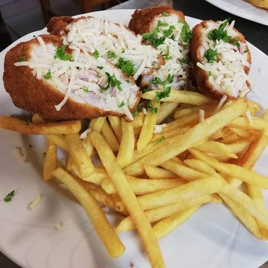 Ein weißer Teller enthält ein golden-braunes gebratenes Hähnchenschnitzel mit Käse und mit Petersilie garniert, begleitet von einer Schicht goldener Pommes Frites.