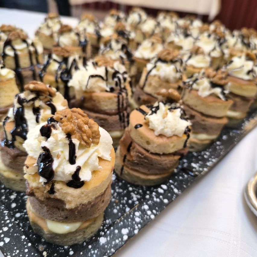 Ein Tablett gefüllt mit kleinen Desserts, jedes mit Schlagsahne, Schokoladensauce und Walnüssen garniert. Die Desserts sind geschichtet und ordentlich gestapelt.