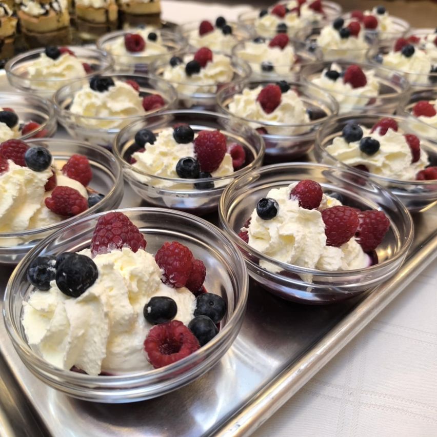 Mehrere Glasbowlen mit Schlagsahne und Beeren, Himbeeren und Blaubeeren. Das Dessert ist auf einem silbernen Tablett angeordnet.