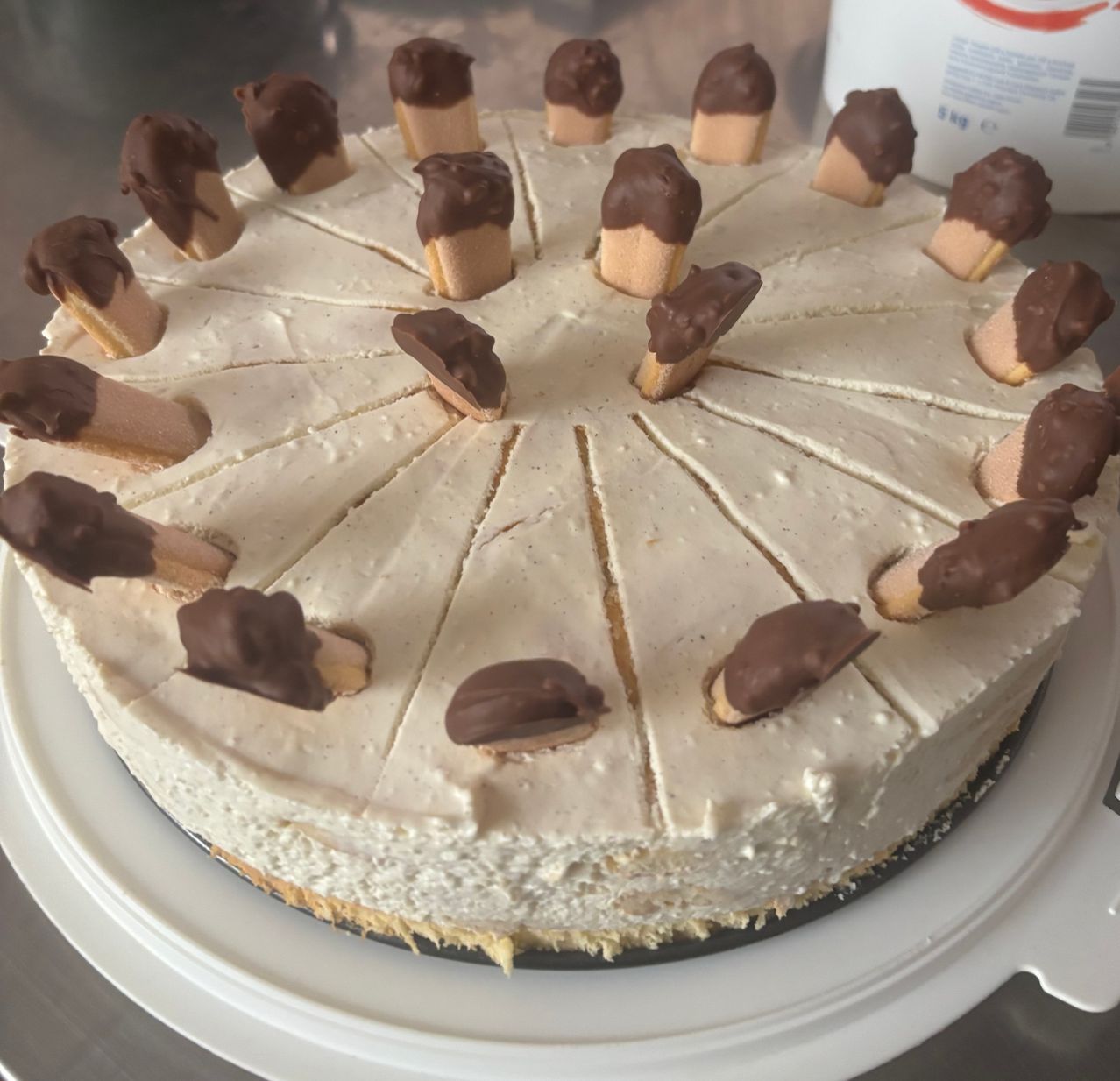 Ein Käsekuchen ist mit Vanilleeis-Zapfen, die mit Schokolade überzogen sind, gekrönt und in einem Kreis angeordnet. Der Kuchen steht auf einem weißen Teller.