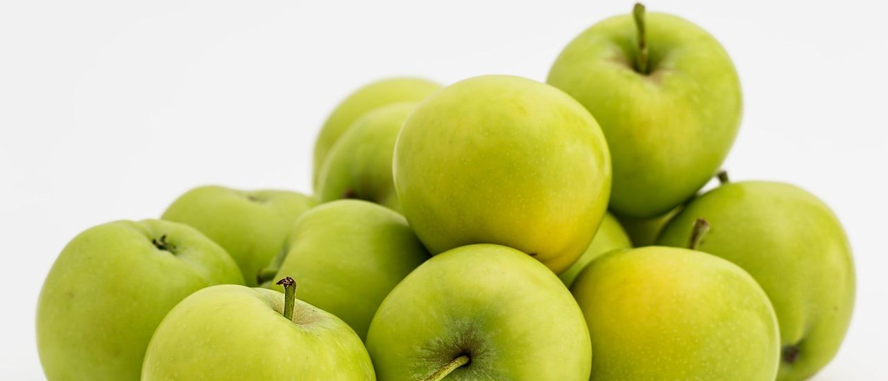 Eine Ansammlung grüner Äpfel mit einem gelben Schimmer, auf einem weißen Hintergrund angeordnet, zeigt ihre runde Form und feste Textur.