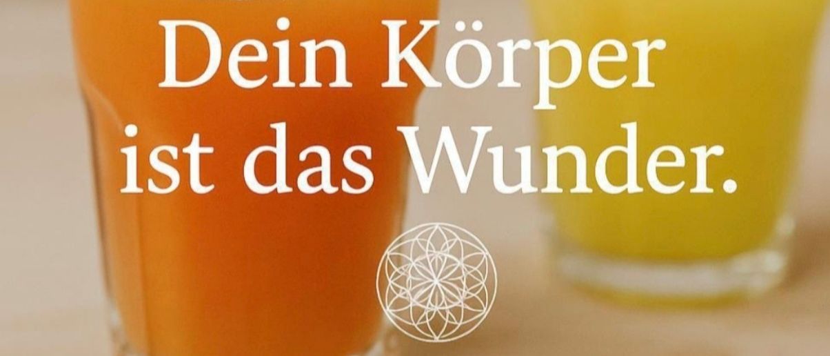 Zwei Gläser mit Saft und einem Blumendesign in der Mitte. Ein Glas enthält Karottensaft und das andere Orangensaft. Der Text lautet 'Dein Körper ist das Wunder.' und 'Gib ihm, was er braucht - und er tut, was er soll.'